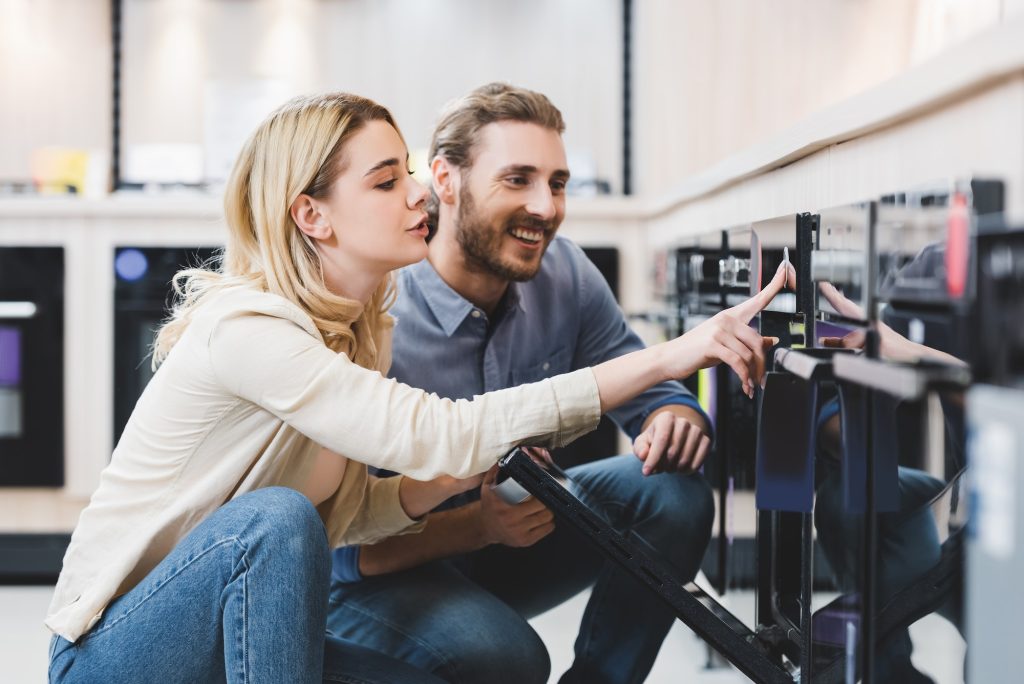 woman using oven and smiling consultant looking at it in home appliance store